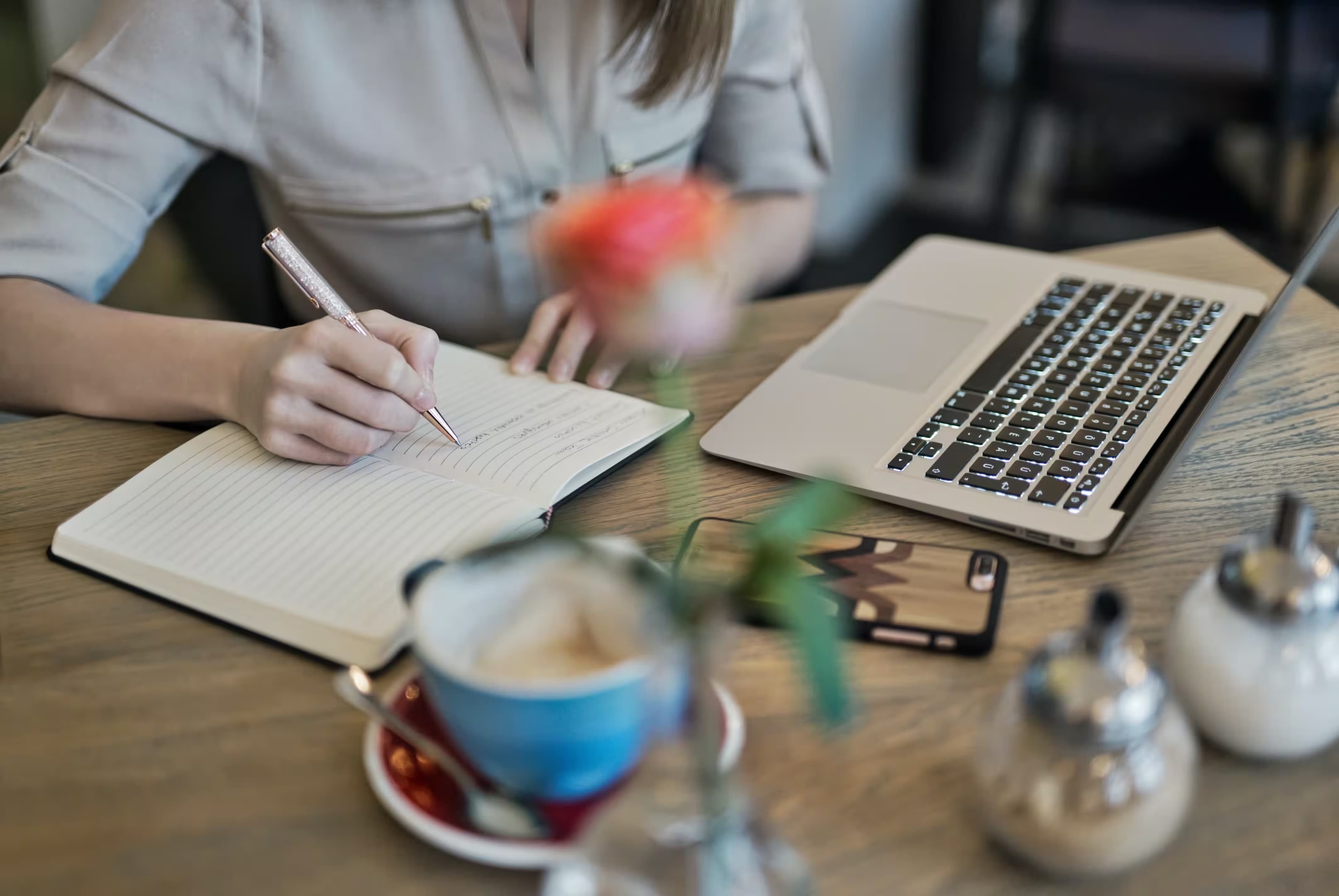 A person sitting at a desk writing notes from a laptop